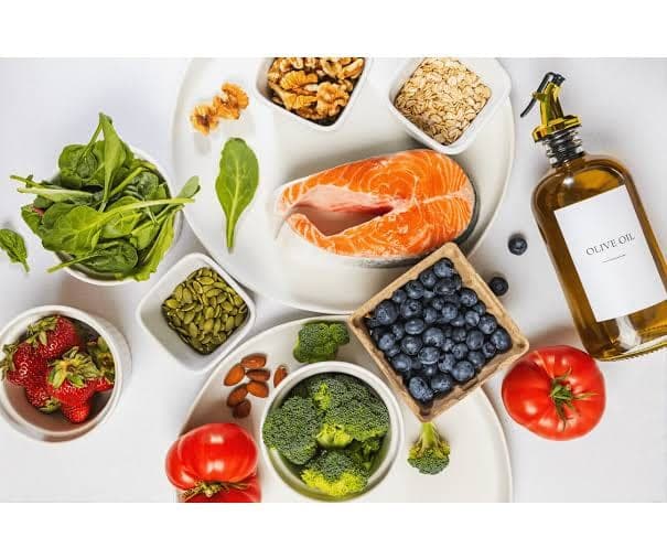 Selección de alimentos antiinflamatorios: salmón, vegetales verdes, frutos rojos, frutos secos y aceite de oliva